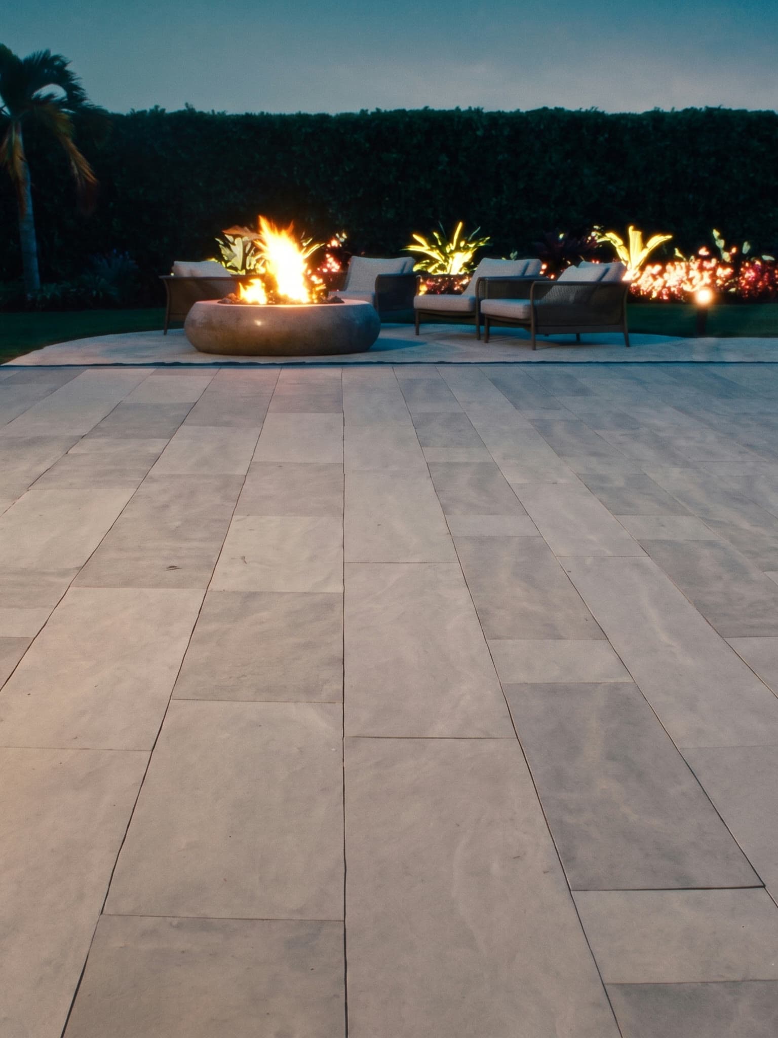Back patio with a fire pit at dusk, paved in 20mm sintered stone pavers in color 6606, a warm greige